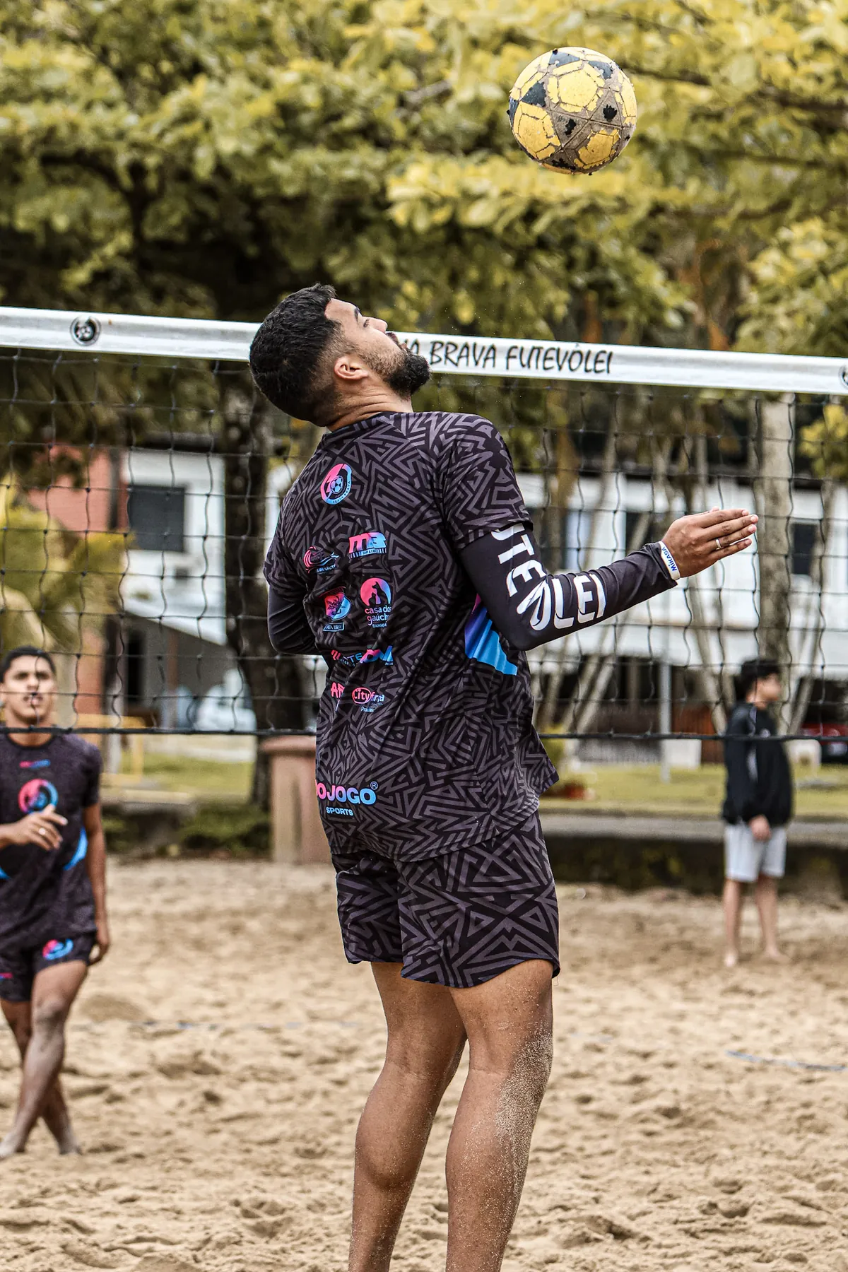 Atleta do CT olha para a bola no alto, junto à rede do Praia Brava Futevôlei